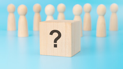 Sticker - wooden cube with question mark are placed on a blue table amid wooden figurines, representing business and education. the close-up focuses on the cubes