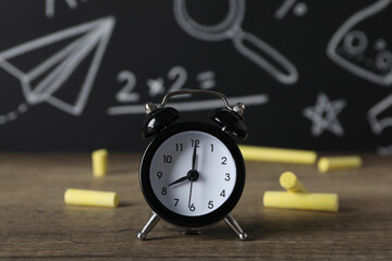 Wall Mural - A black alarm clock on the background of a school blackboard