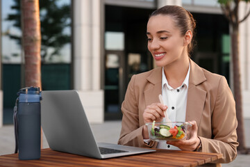 Wall Mural - Happy businesswoman using laptop during lunch at wooden table outdoors