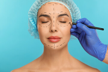 Wall Mural - Doctor with pencil preparing patient for cosmetic surgery operation on light blue background, closeup