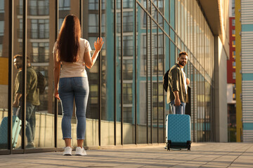 Wall Mural - Long-distance relationship. Woman waving to her boyfriend with luggage near building outdoors