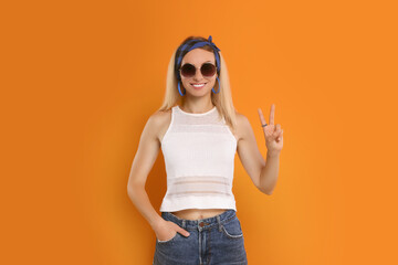 Poster - Smiling hippie woman showing peace sign on orange background