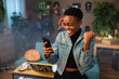 © ABCreative - Happy african american teen girl lady woman with short hair using cell phone holding in hands smiling celebrating raising fists.
