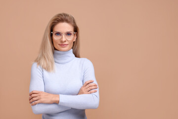 Canvas Print - Portrait of beautiful middle aged woman in glasses with crossed arms on beige background. Space for text