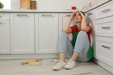 Sticker - Tired woman sitting on dirty floor with utensils and food leftovers in messy kitchen