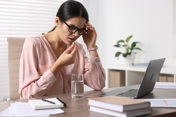 Canvas Print - Young woman with pill and glass of water suffering from headache at wooden table in office