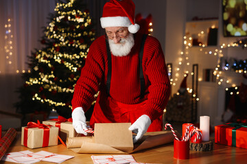 Poster - Santa Claus wrapping gift at his workplace in room decorated for Christmas