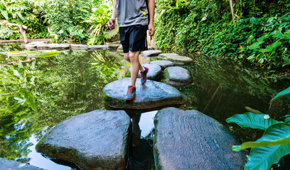 Wall Mural - Young man walking crossing a river on stones