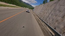 Follow view white sports car speed riding under bridge on serpentine asphalt road summer mountain landscape alpine sunny resort. FPV drone flying over fast automobile surrounded by nature scenery 4k