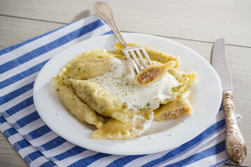 Wall Mural - cooked dumplings with meat, spices and sour cream, in a plate on a light wooden table.