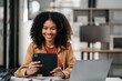 © NINENII - Black businesswoman sits in a office working on tablet play social media.