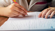 © Angela - Close nas mãos de uma criança que está a escrever em um caderno. Conceito de volta às aulas.