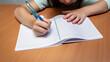 © Angela - Close nas mãos de uma criança que está a escrever em um caderno. Conceito de volta às aulas.