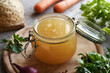 A jar of chicken bone broth or soup with fresh vegetables