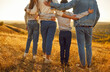 © Studio Romantic - Back view cropped photo of family hugging and looking into the distance enjoying sunset and beautiful nature standing in a row together. Young parents with children walking outdoors.