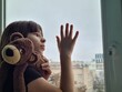 © Nadzeya - Lonely little girl hugs toy and looks out window