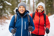 Happy mature multiethnic girlfriends training Nordic walking with ski trekking poles in winter forest
