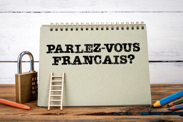 Wall Mural - Do you speak french? Written in French. Green notepad on wooden texture table and white background
