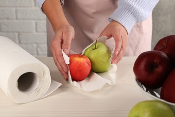 Wall Mural - Woman wiping apples with paper towel at light wooden table, closeup