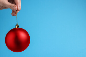 Wall Mural - Woman holding red Christmas ball on light blue background, closeup. Space for text