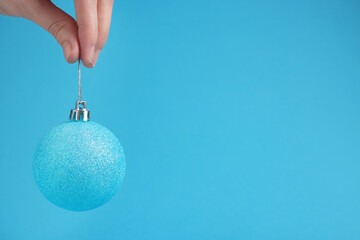 Wall Mural - Woman holding glitter Christmas ball on light blue background, closeup. Space for text