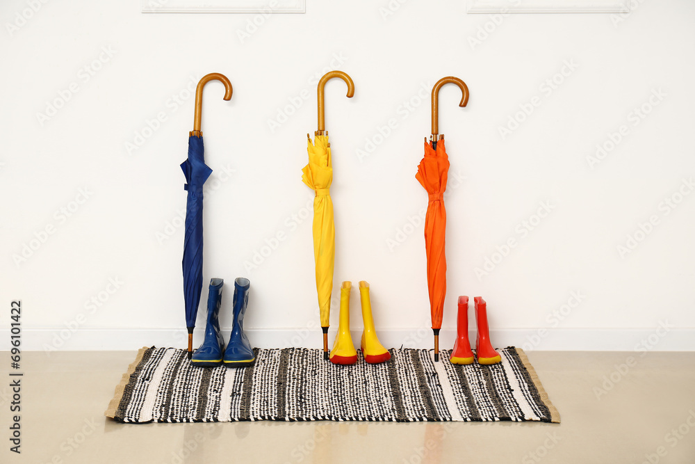 Colorful umbrellas and rubber boots near light wall
