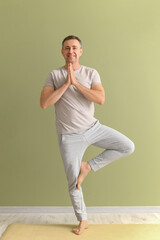 Poster - Mature man doing yoga on mat near green wall