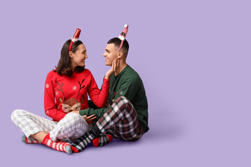Wall Mural - Happy young couple in Christmas pajamas on lilac background