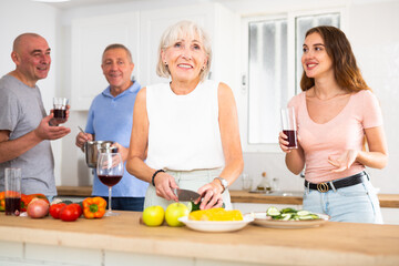 Wall Mural - Happy family of four with glasses of wine in their hands is preparing a festive dinner in a home kitchen