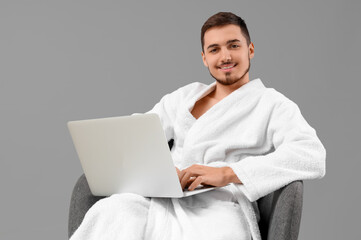 Poster - Handsome young man in bathrobe with laptop on grey background