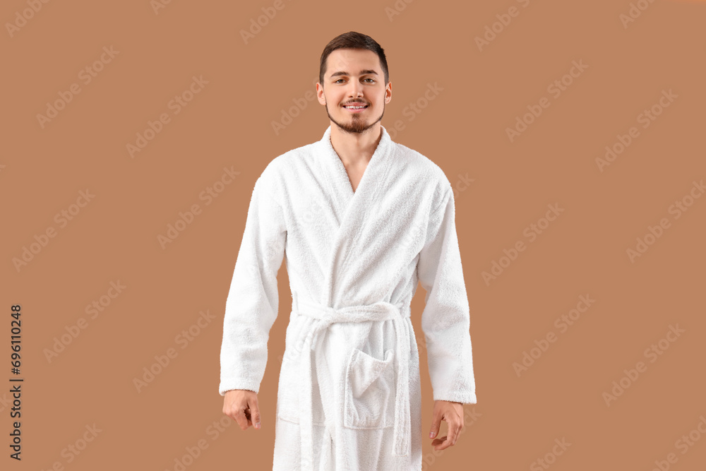 Handsome young man in bathrobe on beige background