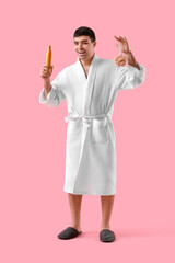 Poster - Handsome young man in bathrobe with bath sponge and shower gel on pink background