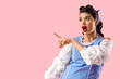 Shocked young pin-up woman pointing at something on pink background
