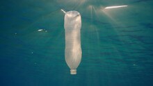 Disposable Plastic Bottle Drift Under Surface Of Water In Bright Sunrays. A Plastic Bottle Is Thrown Into The Sea Slowly Drifts In Water Column In Rays Of Morning Sun, Red Sea, Egypt, Africa