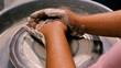 Close-up of a female potter's hands at work moulding a work of art from white clay on a potter's wheel. The concept of manual labour, art and craftsmanship.
