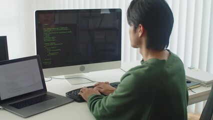 Rear view of male back-end developer writing code while sitting in front of computer at office