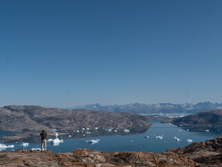 Eine Mann blickt auf einen Fjord mit Eisbergen in Grönland.