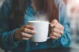 Fototapeta  - In the morning, a young woman holds a hot cup of tea or coffee in her hands.