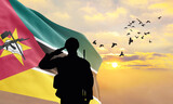 Fototapeta  - Silhouette of a soldier with the Mozambique flag stands against the background of a sunset or sunrise. Concept of national holidays. Commemoration Day.
