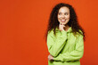 © ViDi Studio - Young fun woman of African American ethnicity she wear green hoody casual clothes put hand prop up on chin, lost in thought and conjectures isolated on plain red orange background. Lifestyle concept.