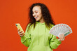 © ViDi Studio - Young smiling woman of African American ethnicity she wear green hoody casual clothes hold in hand fan of cash money in dollar banknotes use mobile cell phone isolated on plain red orange background.