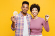 © ViDi Studio - Young couple two friends family man woman of African American ethnicity wear purple casual clothes together hold in hand bunch of keys wooden house mockup isolated on plain yellow orange background.
