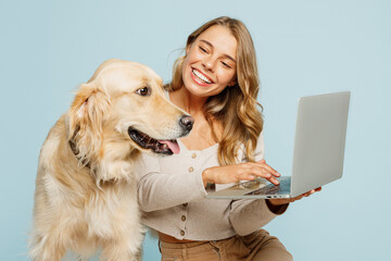 Wall Mural - Young happy owner IT woman with her best friend retriever dog wear casual clothes hold use work on laptop pc computer isolated on plain pastel light blue background studio Take care about pet concept