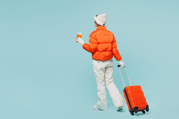 Traveler skier woman wear padded windbreaker jacket ski goggles mask hold passport ticket bag go isolated on plain blue background Tourist travel abroad in free time rest getaway. Air flight concept.