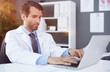 © Katsiaryna - Focused doctor sitting at his desk using his laptop
