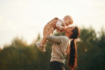 Holding kid in hands. Mother is with her little baby son are outdoors together