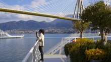 Woman On A Ferry Boat Looking At Iconic Patras Rio Antirio Bridge In Greece With Other Boats On The Water