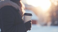Woman In Winter Jacket Holding Paper Cup Of Coffee On A Street In Cold Morning Light