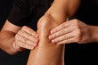A masseur gives a knee massage to a girl on a dark background, massage of the knee joint