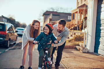 Happy young boy having first bike ride with parents outside